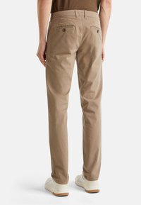 Beige Baumwollhose mit zwei Gesäßtaschen, sichtbaren Nähten und geradem Bein. Kombiniert mit weißen Sneakern.