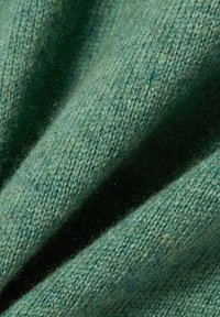 Textil mit einer weichen, gewebten Textur in einem gedämpften Grünton. Der Stoff weist feine Farbabstufungen und ein feines Strickmuster auf.