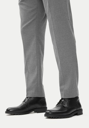 Fekete bőrcipők sima felülettel, lekerekített orral és fűzős részletekkel. Szürke nadrággal párosítva, amely texturált anyagból készült.