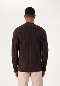Pull en tricot marron foncé avec une texture côtelée et un motif torsadé, manches longues et col rond. Vue de dos.