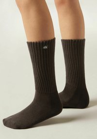 Dunkelbraune, gestrickte Socken mit einem gerippten Bund. Das Material zeigt eine weiche Textur und hat ein kleines "clz"-Logo an der Seite.