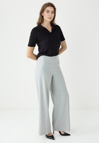 Zwarte polo met korte mouwen, gecombineerd met lichtgrijze wijde broekpoten en zwarte puntige hakken, met een gladde textuur en een op maat gemaakte uitstraling.