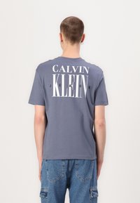 Hall halli puuvillane t-särk lühikeste varrukatega, mille seljal on suur valge "CALVIN KLEIN JEANS" kiri. Pehme tekstuur, juhuslik lõige.