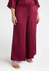 Kastanjefärgade vida byxor med elastiskt midjeband och dragsko. Tillverkade av ett mjukt, lätt tyg. Bärs med lätta sandaler.