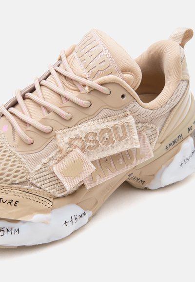 Μπεζ αθλητικό παπούτσι με ανάμεικτα υλικά, χοντρή σόλα με χειρόγραφες σημειώσεις, υφασμάτινα μπαλώματα με την επωνυμία "Dsquared2" και μπεζ κορδόνια.