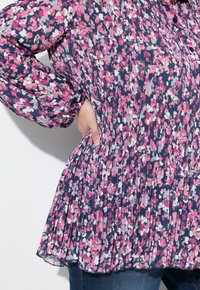 Blusa floral con tejido plisado, que presenta tonos de rosa, blanco y azul marino. Mangas largas abullonadas con puños elásticos y dobladillo redondeado.