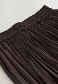 Falda plisada de color marrón oscuro con una cintura smock. Presenta un tejido texturado con un sutil brillo y plisados verticales en toda la prenda.