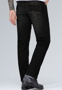Jeans de mezclilla negra con corte recto, bolsillos traseros visibles, costuras en contraste y un dobladillo estrecho, combinados con botas de tobillo grises.