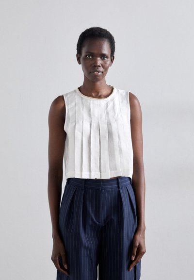 Cropped white pleated top with a round neckline, paired with navy pinstriped high-waisted trousers featuring front pleats and side pockets.