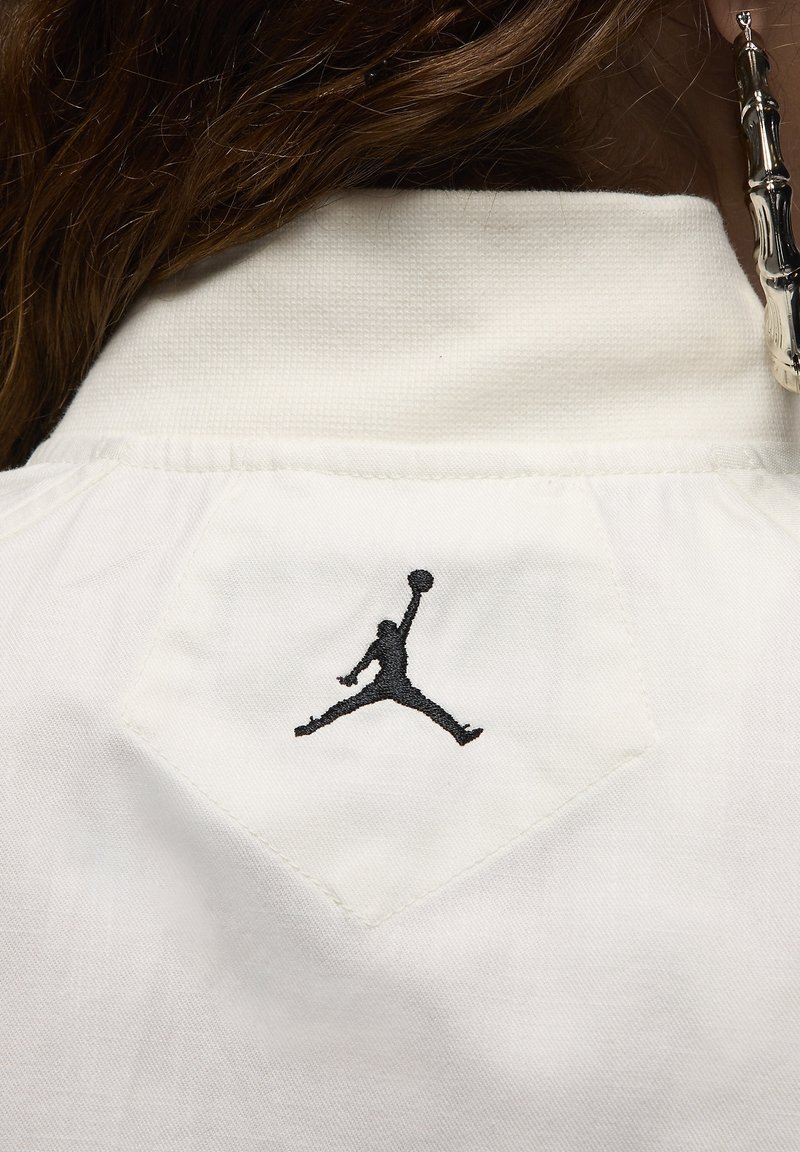 Col blanc avec un logo Jumpman noir brodé, présentant une finition texturée et un patch en forme de diamant à l'arrière.