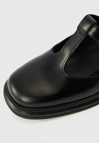 Μαύρο δερμάτινο παπούτσι με στρογγυλεμένη μύτη, κομμένες πλευρές και λεία υφή. Διαθέτει χαμηλή ελαστική σόλα και λεπτές ραφές.