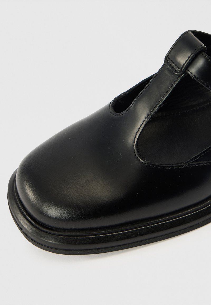 Schwarzer Lederschuh mit abgerundetem Zehenbereich, ausgeschnittenen Seiten und glatter Textur. Verfügt über eine flache Gummisohle und dezente Steppnähte.