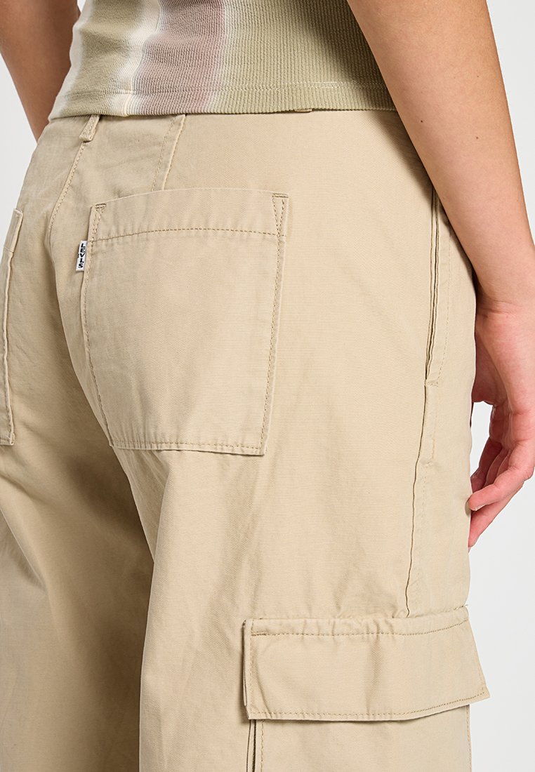 Pantalones cargo beige hechos de un tejido duradero, con múltiples bolsillos y costuras visibles. Textura suave con un diseño de ajuste relajado.
