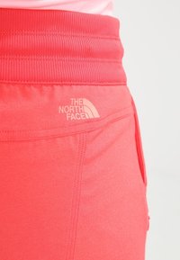 Pantalones cortos deportivos rojos con una cintura acanalada, que presentan el logo de "The North Face" en rosa claro. Hechos de tela suave y elástica con bolsillos laterales.