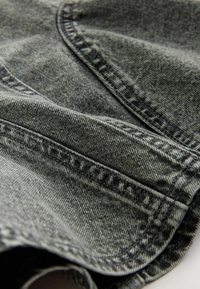 Tessuto denim grigio con cuciture visibili, texture sottile e cuciture curve. Il materiale presenta un leggero motivo strappato e una superficie liscia.