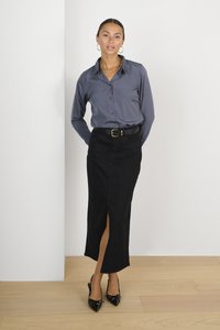 Chemise grise à boutons, jupe noire ceinturée avec une fente sur le côté, et escarpins noirs à bout pointu. Tissu lisse et coupe ajustée. Arrière-plan clair.