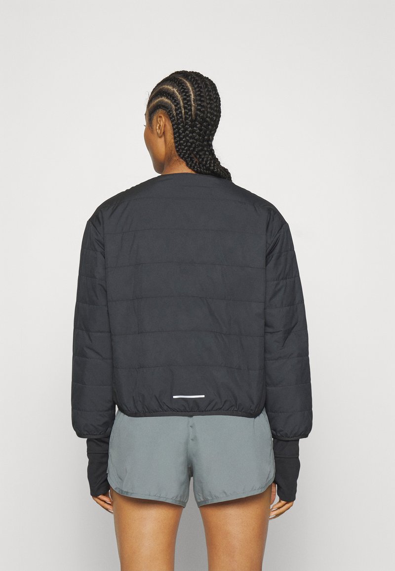 Schwarze gesteppte Jacke mit Rundhalsausschnitt, langen Ärmeln und deastischem Bund; verfügt über einen reflektierenden Akzent auf der Rückseite.