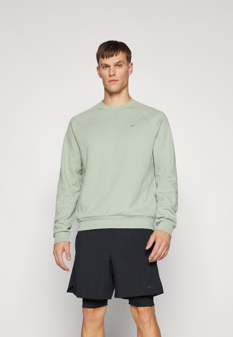 Felpa verde chiaro con collo rotondo e maniche raglan, abbinata a pantaloni corti neri. Presenta il logo Nike sul petto. Tessuto morbido.