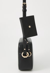 Schwarze Lederhandtasche in zylindrischer Form, mit einem abnehmbaren Kartenhalter, goldenen Hardware-Elementen und einer strukturierten Oberfläche.