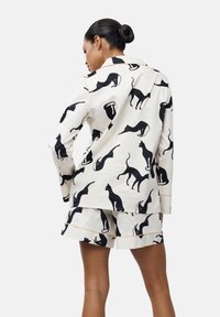 Set di pigiama in cotone con uno sfondo bianco e silhouette nere di cani. La parte superiore ha un colletto e maniche lunghe, mentre i pantaloni corti sono di lunghezza media.