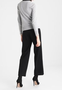 Grå, figursydd tröja med långa ärmar, med knappdetaljer vid manschetterna, kombinerad med svarta vida byxor och svarta högklackade skor.