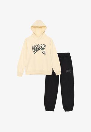 Felpa crema con stampa grafica in verde e nero, abbinata a pantaloni della tuta neri con un piccolo logo. Entrambi realizzati in tessuto di cotone.