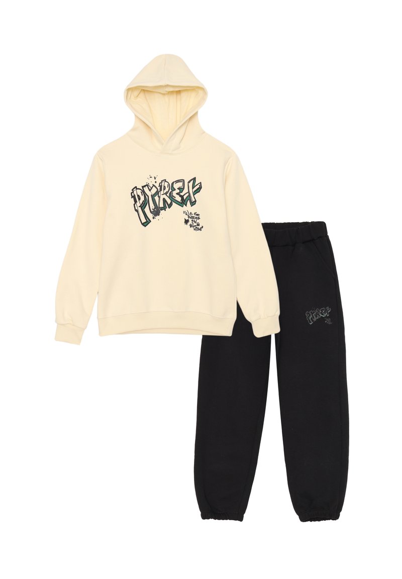 Felpa crema con stampa grafica in verde e nero, abbinata a pantaloni della tuta neri con un piccolo logo. Entrambi realizzati in tessuto di cotone.