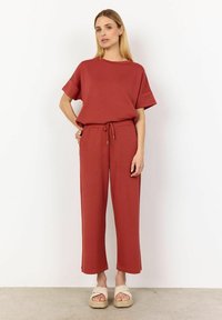 Roodbruine katoenen top met een mix van stoffen en korte mouwen, gecombineerd met bijpassende broek met trekkoorden. Glad textuur en een ontspannen pasvorm; gedragen met platte sandalen.