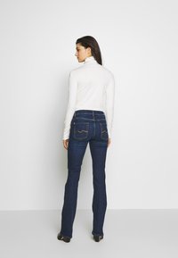 Donkerblauwe denim flared jeans met gestikte achterzakken, gecombineerd met een nauwsluitend wit longsleeve shirt. Glad textuur, slim fit.