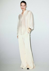 Light beige blouse with a relaxed fit and shiny texture, paired with ivory wide-leg pants and black heels, featuring subtle details and cuff accents.