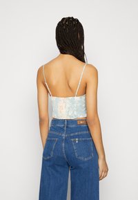 Top cropped florido em azul claro com banda elástica, alças finas e textura suave, combinado com calças de ganga de cintura alta.