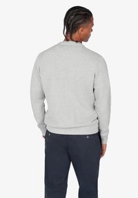 Sudadera gris con una superficie texturizada, cuello redondo y puños y dobladillo de canalé. Lleva pantalones oscuros, vista desde atrás.