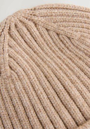Bonnet en tricot côtelé beige avec une texture douce et un sommet arrondi. Le design comprend des lignes verticales en relief et un bord fini.