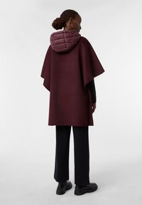 Burgundowy poncho z pikowaną, fioletową kapturem. Luźny krój, gładka faktura, z bocznymi otworami i tradycyjną sylwetką.