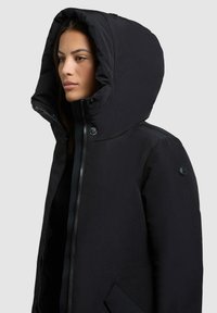 Zwarte capuchonjack met een ritssluiting aan de voorkant, drukknoopsluitingen, elastische manchetten en zijzakken; gladde stof met minimale details.