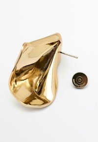 Boucle d'oreille métallique dorée avec une forme fluide et organique et une surface texturée ; comprend un disque de support marqué.