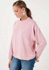 Felpa rosa con collo alto e maniche lunghe, caratterizzata da una vestibilità comoda e una texture morbida. Abbinata a jeans blu.