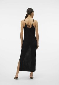 Abito maxi in maglia nera con spalline sottili, design con schiena scoperta, spacco laterale e tessuto testurizzato, abbinato a sandali neri con cinturini.