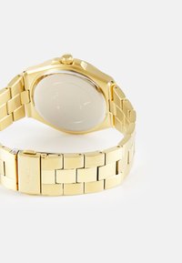 Montre-bracelet en métal doré avec un bracelet à maillons et un boîtier texturé. Présente une lunette arrondie et un dos lisse et réfléchissant.