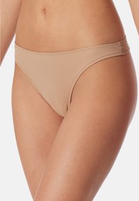 Beżowe slipy bikini wykonane z gładkiego materiału, charakteryzujące się niskim stanem oraz wąskimi bokami z subtelnymi detalami stębnowania.