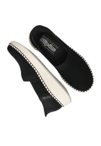 Zwarte gebreide instapschoenen met een gestructureerde bovenkant, witte rubberen zool en contrasterende stikseldetails. "Skechers Slip-Ins" merk zichtbaar aan de binnenkant.