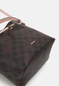 Hnědá kostkovaná kabelka s hladkou texturou, zlatými kovovými prvky a růžovým koženým popruhem. Název značky viditelný na boku.