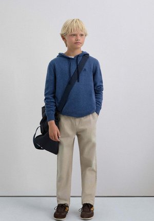 Sudadera con capucha de tela azul oscuro, pantalones beige, zapatos marrones y un bolso de hombro negro. Diseño sencillo con un bolsillo delantero y cordón ajustable.