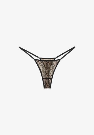 Un string en dentelle noire translucide avec des double fine sangles et un motif circulaire sur le tissu, sur fond blanc.