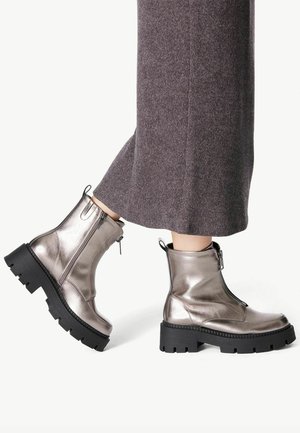 Botines metálicos plateados con una suela de goma negra gruesa, cierre lateral y detalle de tira para poner. Combinados con unos pantalones de punto grises.