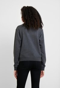 Sudadera gris hecha de una suave mezcla de algodón, con un ajuste relajado, puños y dobladillo acanalados. La vista trasera muestra detalles de costura mínimos.