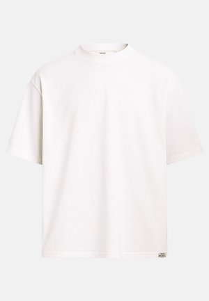 T-shirt blanc uni à manches courtes et col rond, avec une petite étiquette rectangulaire "Rebel" sur l'ourlet inférieur droit.