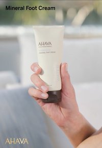 Krem do stóp mineralny w jasnobeżowej tubce z ciemnobrązową nakrętką. Etykieta zawiera napis "AHAVA" oraz "MINERAL FOOT CREAM", gładka konsystencja.