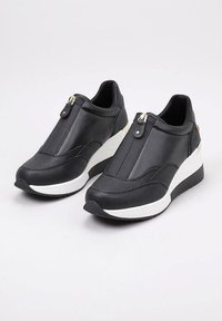 Zapatillas negras con cuña, con paneles texturizados y lisos, cierre de cremallera en el frente y suela blanca gruesa sobre un fondo blanco.