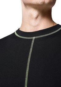 Czarna koszulka sportowa z zielonymi przeszyciami; ma okrągły dekolt i pionowy szew na przodzie. Gładka tekstura materiału.